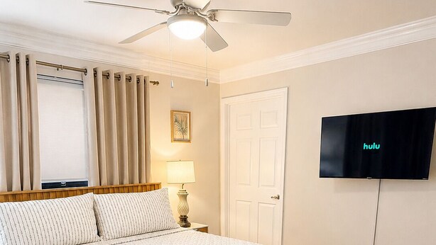 A bedroom with a bed, a ceiling fan, a television, and a door. - Spacious 5-bedroom Modern Retreat with Heated Pool Near Beach and Cove Shopping (Deerfield Beach)