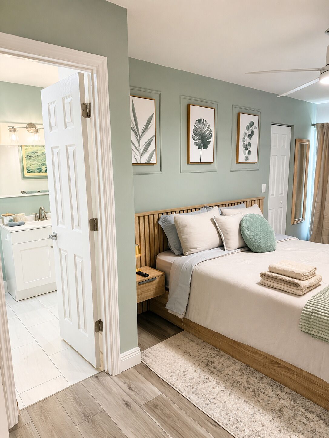 Une chambre à coucher comprenant un lit, des tables de chevet, une commode, un miroir et une porte donnant accès à une salle de bain.