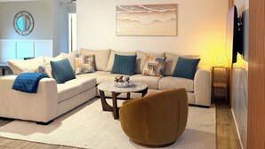 A modern living room with a sectional sofa, a round coffee table, and a brown accent chair. - Spacious 5-bedroom Modern Retreat with Heated Pool Near Beach and Cove Shopping (Deerfield Beach)
