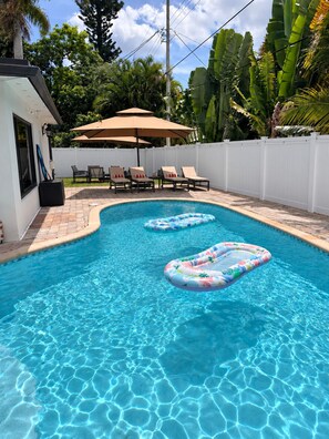 A swimming pool with two inflatable rings, a white fence, and a covered seating area with chairs and an umbrella. - Spacious 5-bedroom Modern Retreat with Heated Pool Near Beach and Cove Shopping (Deerfield Beach)