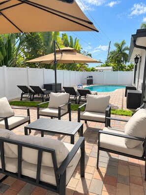 Un jardin avec une piscine, du mobilier d’extérieur et une clôture blanche.
