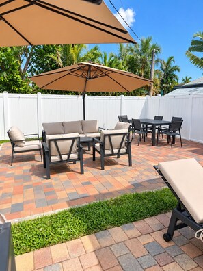 An outdoor patio with a sofa set, dining table, and chairs, surrounded by a white fence and palm trees. - Spacious 5-bedroom Modern Retreat with Heated Pool Near Beach and Cove Shopping (Deerfield Beach)