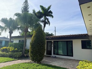 A residential property with a paved driveway, a well-maintained lawn, and a variety of trees including palm trees.