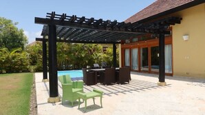 Ein überdachter Außenbereich mit Pool, grünen Stühlen und einem Tisch.
