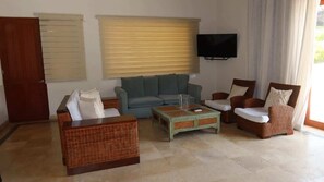 Ein Wohnzimmer mit einer Couch, zwei Sesseln, einem Couchtisch und einem an der Wand befestigten Fernseher.