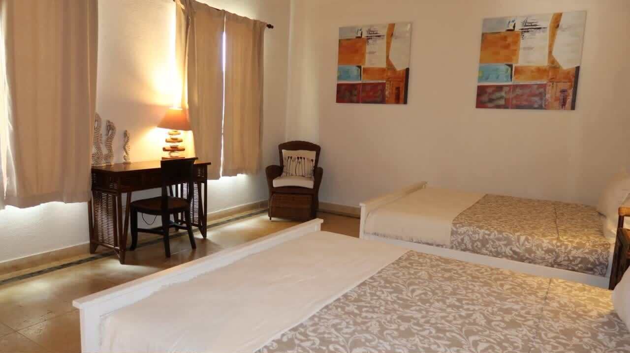 Une chambre avec deux lits, un bureau, une chaise et une lampe.