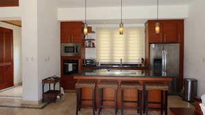 A modern kitchen with a central island, bar stools, stainless steel appliances, and pendant lighting. - Caribbean bungallow with 2 bedrooms in Cap Cana (Punta Cana)