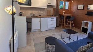 En kompakt opholdsstue med et tekøkken, spiseplads og en sofa.