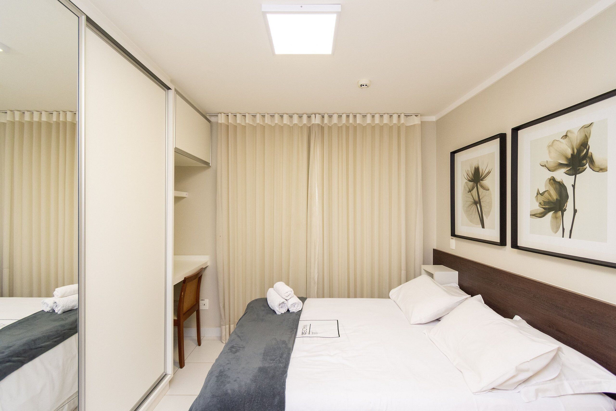 Habitación de hotel con cama, escritorio, silla, espejo y dos cuadros en la pared.