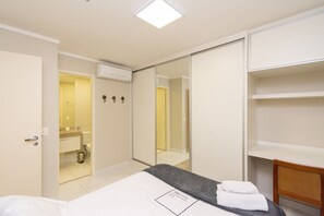 Habitación de hotel con cama, mesita de noche, espejo, armario y baño visible a través de una puerta abierta.