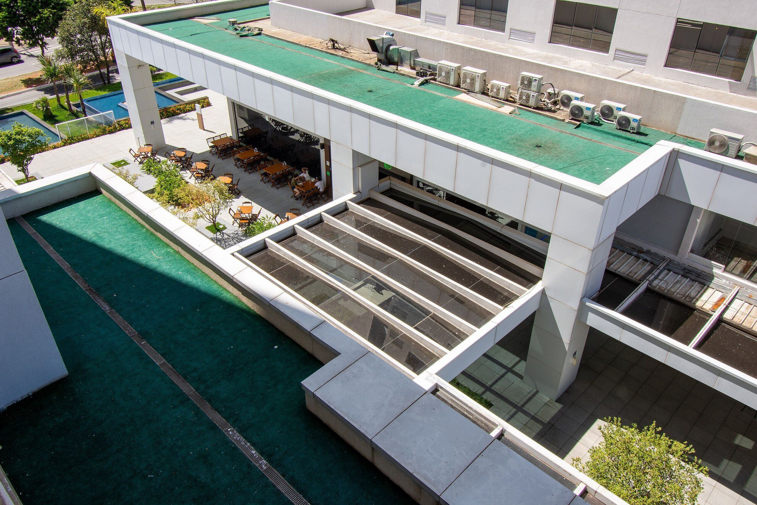 Un edificio moderno con piscina en la azotea, mobiliario exterior y varios equipos de aire acondicionado.