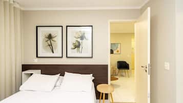 Habitación de hotel con una cama, dos cuadros con flores en la pared, una silla y una puerta que da a otra habitación.
