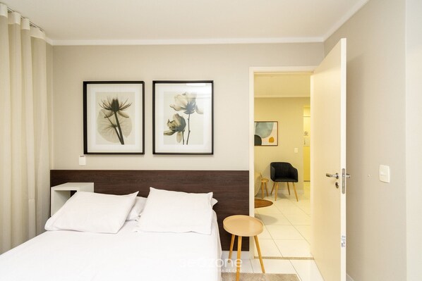 Habitación de hotel con una cama, dos cuadros con flores en la pared, una silla y una puerta que da a otra habitaci ón.