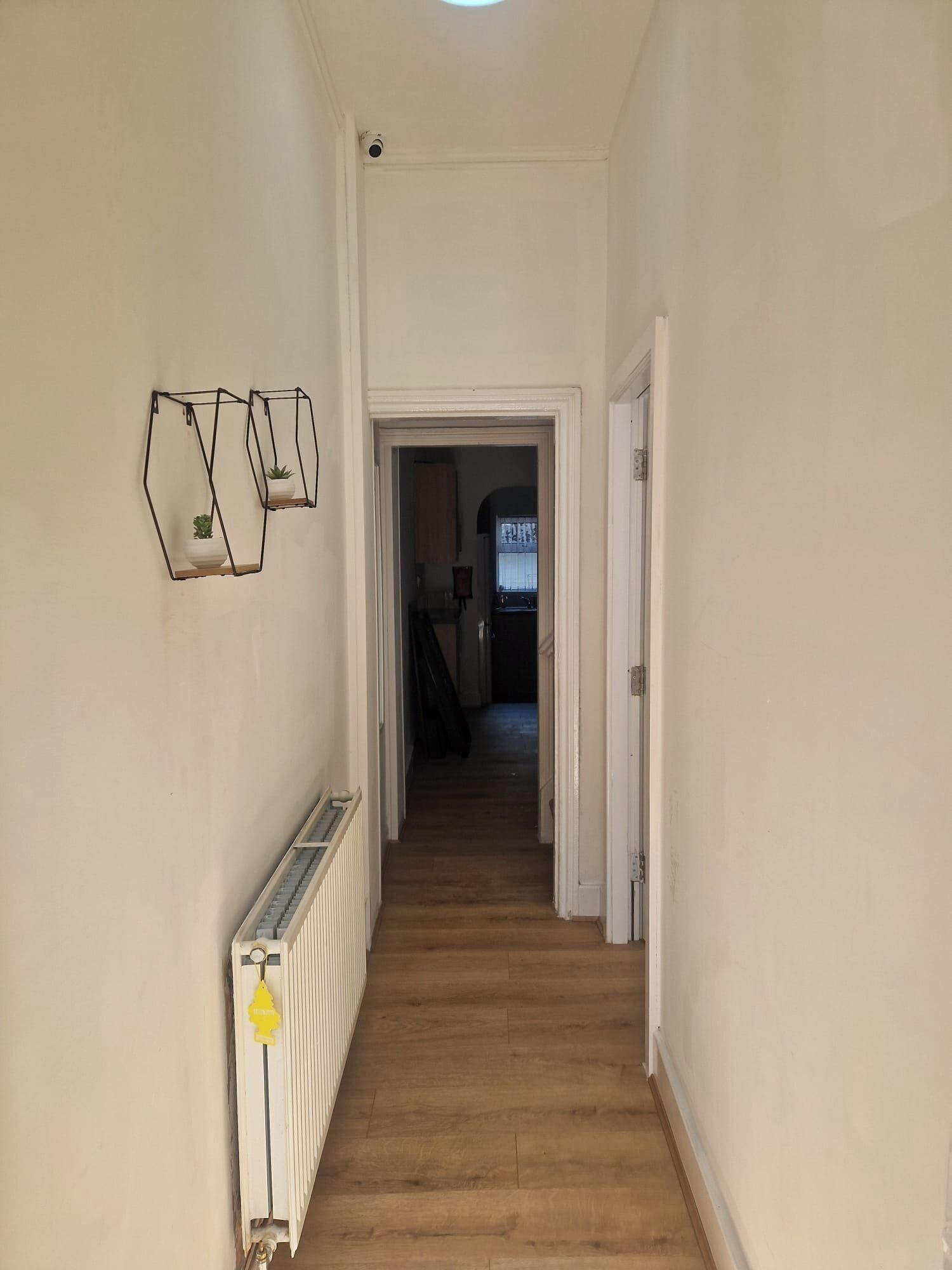 A hallway with a radiator, a door at the end, and a staircase leading to another room.
