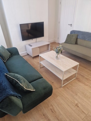 A living room with a green sofa, a coffee table, a TV, and a door in the background. - 3BR House in Barrow-in-Furness | Near transpo | ST (Barrow-in-Furness)