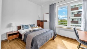 Una camera d'albergo con un letto, un comodino, una lampada e vista su un edificio attraverso una finestra.