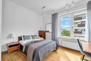 Ein Hotelzimmer mit einem Bett, Nachttisch, Lampe und Blick auf ein Gebäude durch ein Fenster.