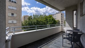 Un balcone con tavolo e sedie, una ringhiera e vista su edifici e alberi.
