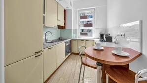 Una cucina compatta con angolo pranzo, una finestra vista edificio e angolo cottura con fornello e lavello.