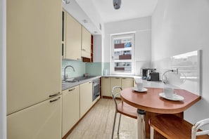 Eine kleine Küche mit Essbereich, ein Fenster mit Blick auf ein Gebäude und eine Küchenzeile mit Herd und Spüle.
