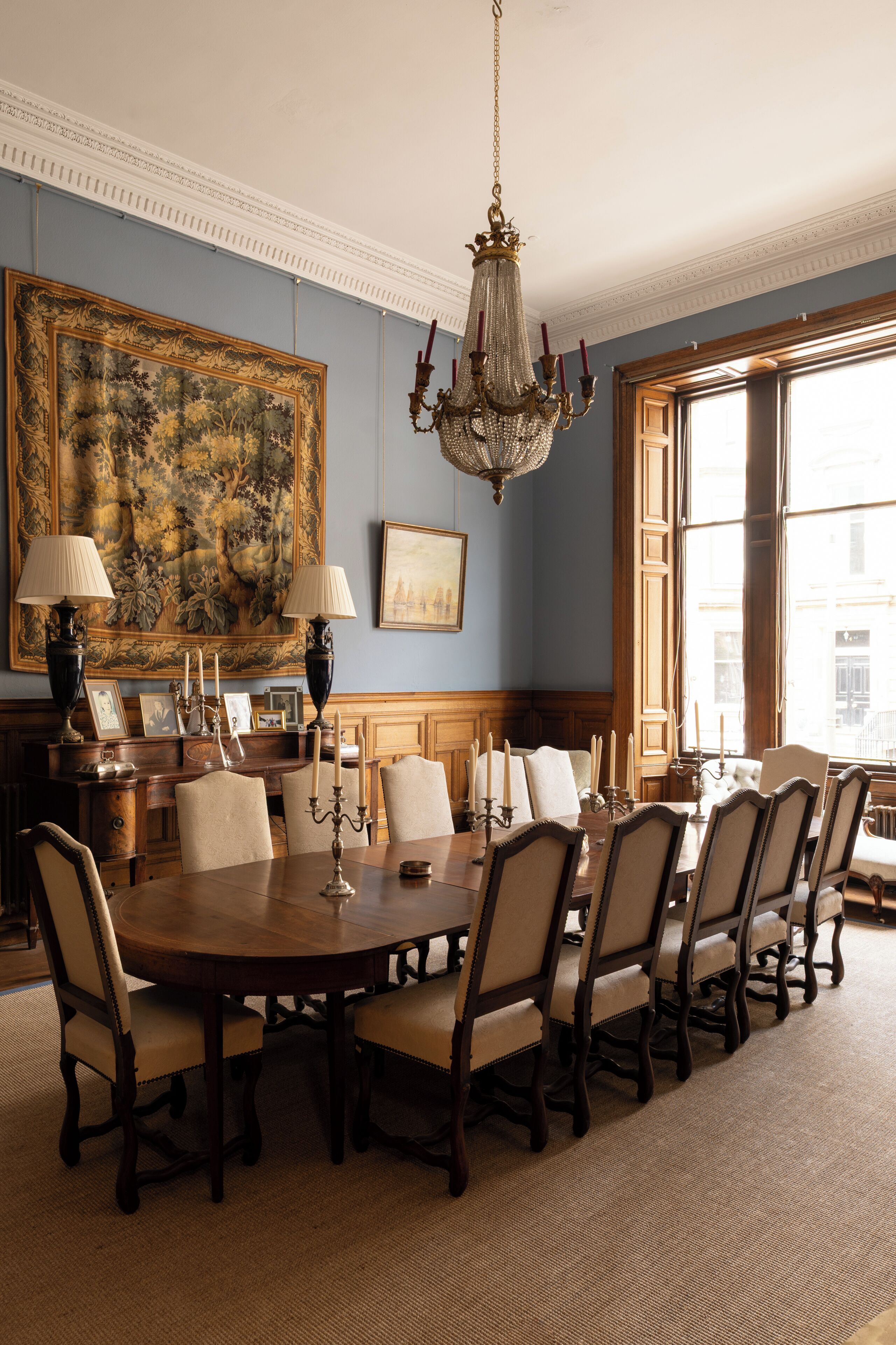 A formal dining room with a large table, chairs, a chandelier, and a large painting on the wall.