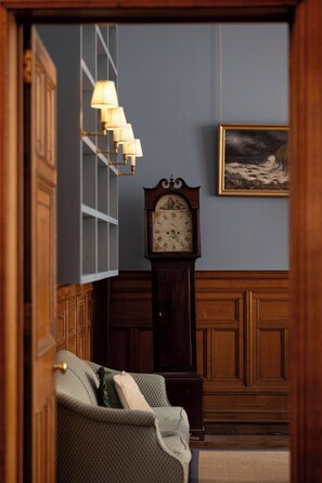 A room with a wooden floor, a large wall clock, a framed painting, and a patterned sofa. - Grand City Centre House (Edinburgh)