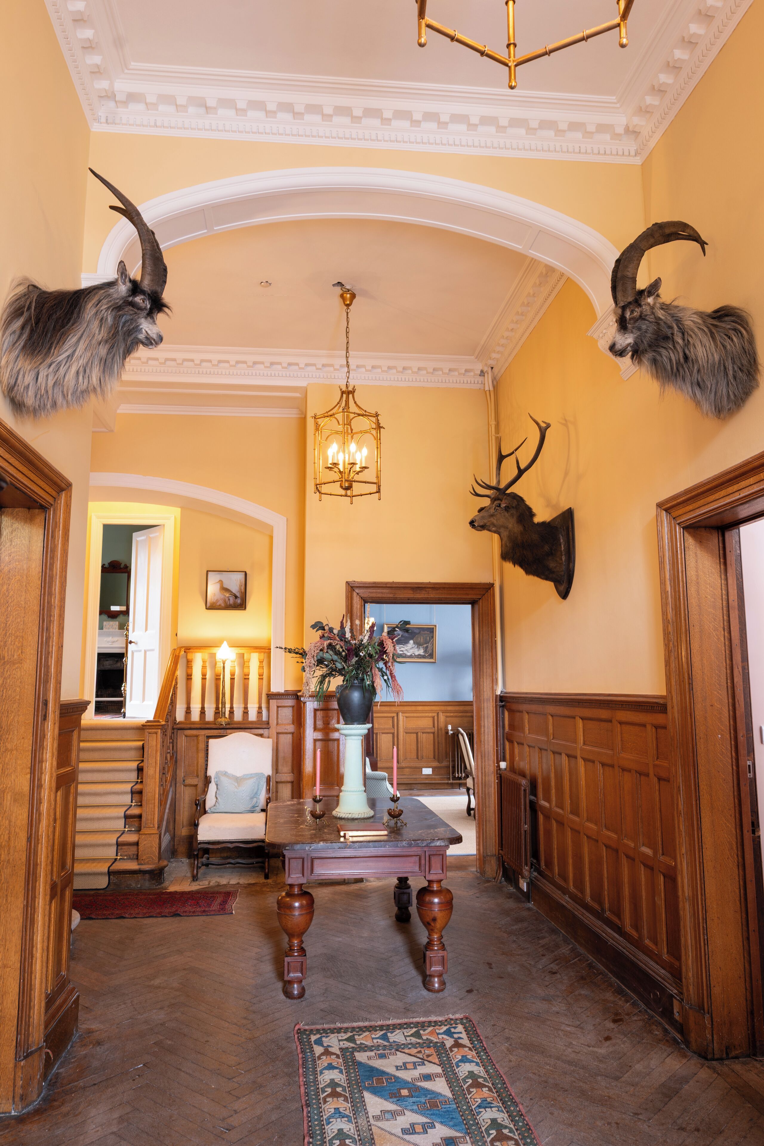 A grand hallway with a chandelier, a fireplace, and mounted animal heads.