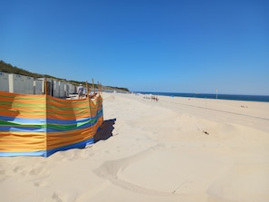 Ein Strand mit einer Reihe von mobilen Toiletten und einer farbenfrohen, gestreiften Markise.