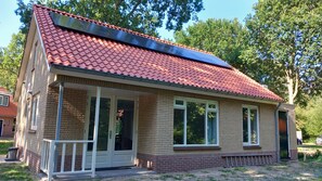 A single-story brick building with a red-tiled roof, large windows, and a covered porch area. - Panda,6-person cottage at the foot of the dunes, a 5-minute walk from the beach. (Vrouwenpolder)