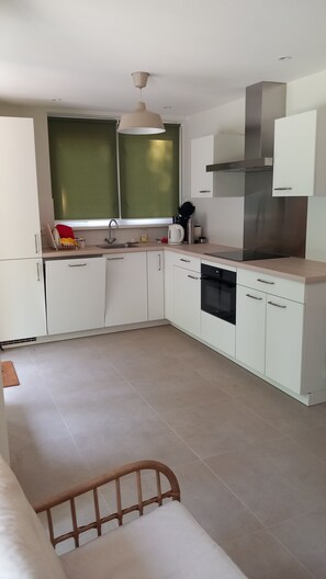 A modern kitchen with white cabinets, a stainless steel range hood, and a window with green blinds. - Panda,6-person cottage at the foot of the dunes, a 5-minute walk from the beach. (Vrouwenpolder)