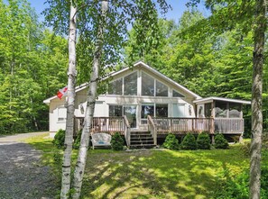A two-story house with a deck, surrounded by trees.