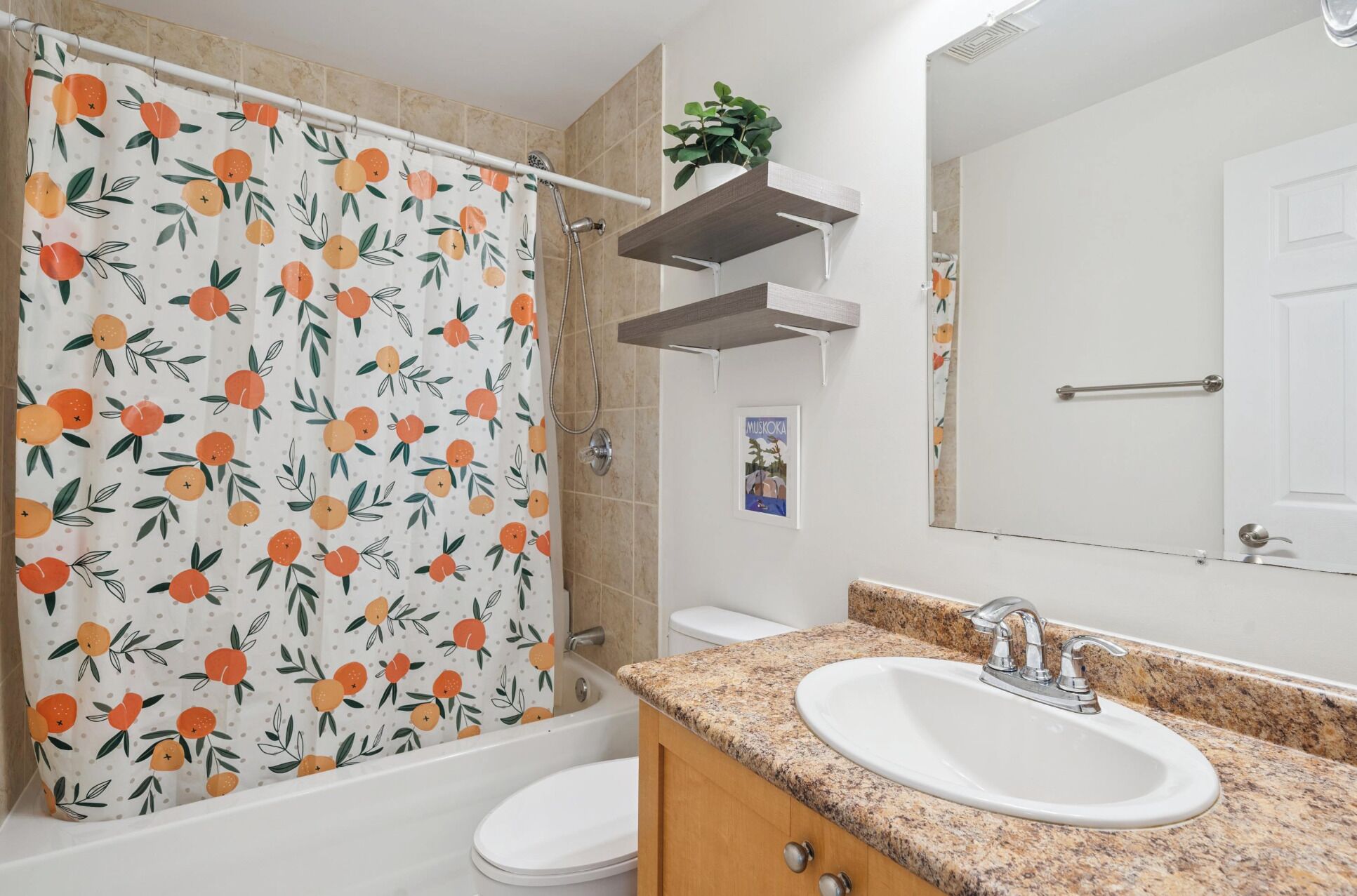 A bathroom with a shower curtain featuring a fruit pattern, a sink with a granite countertop, and a mirror above the sink.