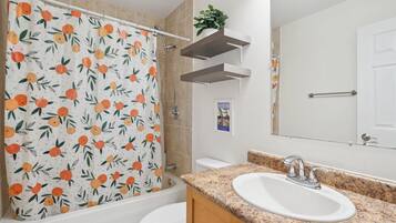 A bathroom with a shower curtain featuring a fruit pattern, a sink with a granite countertop, and a mirror above the sink.