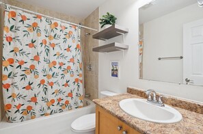 A bathroom with a shower curtain featuring a fruit pattern, a sink with a granite countertop, and a mirror above the sink.