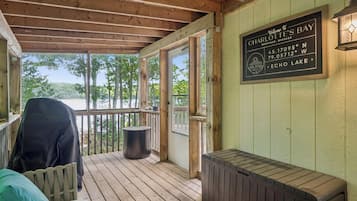 Une terrasse en bois dotée d’un espace salon couvert, une pancarte indiquant qu’on se trouve à Charlotte’s Bay, et une vue sur les arbres et l’eau environnants.
