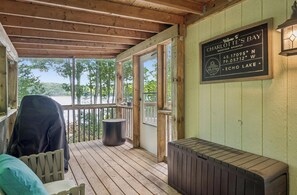 Una terraza de madera con zona de estar cubierta, un cartel que indica el lugar como Charlotte's Bay, y vistas de los árboles y el agua circundantes.