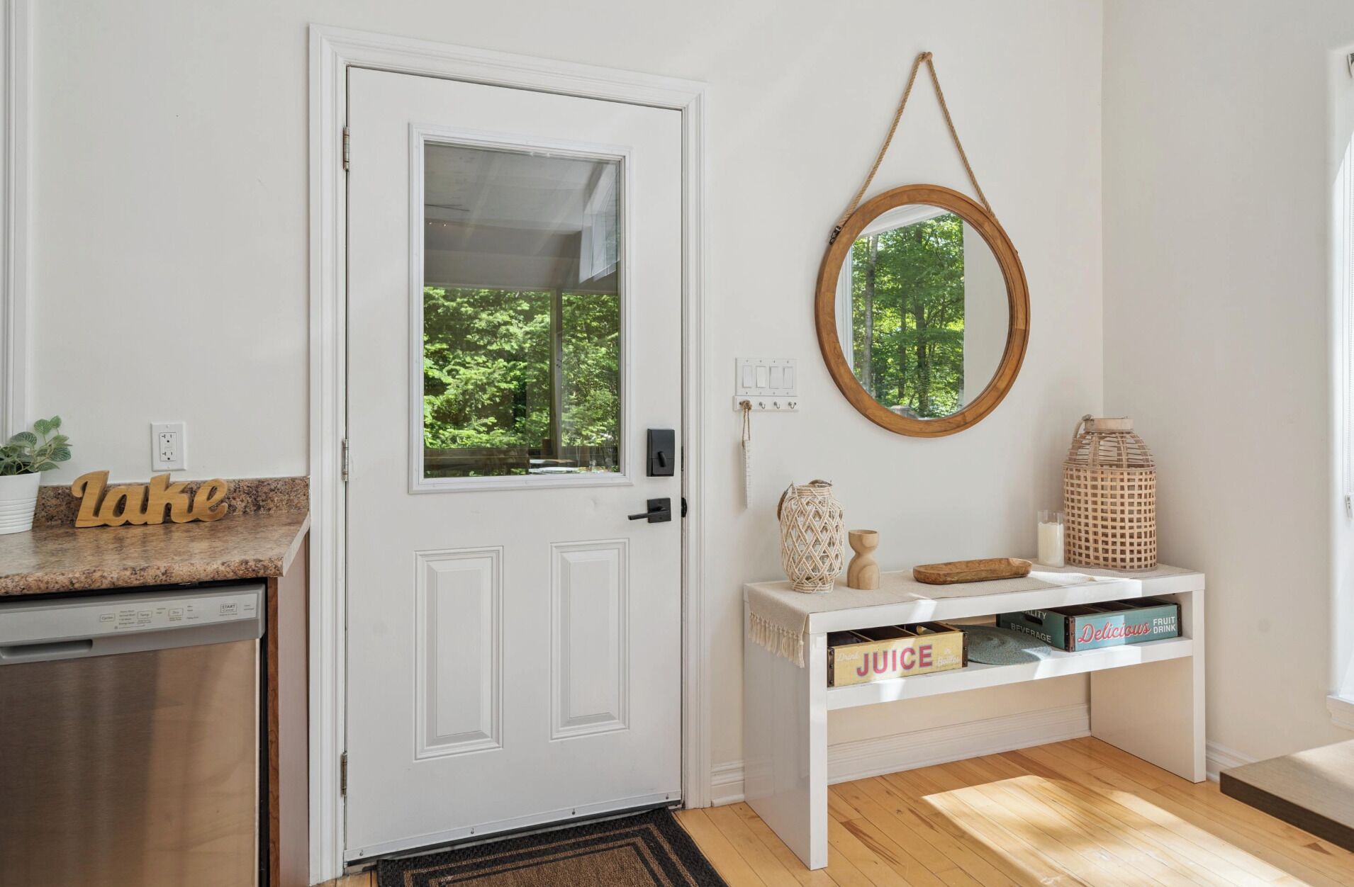 A kitchen with a white door, a window, a wooden sign, a white console table, and a mirror.