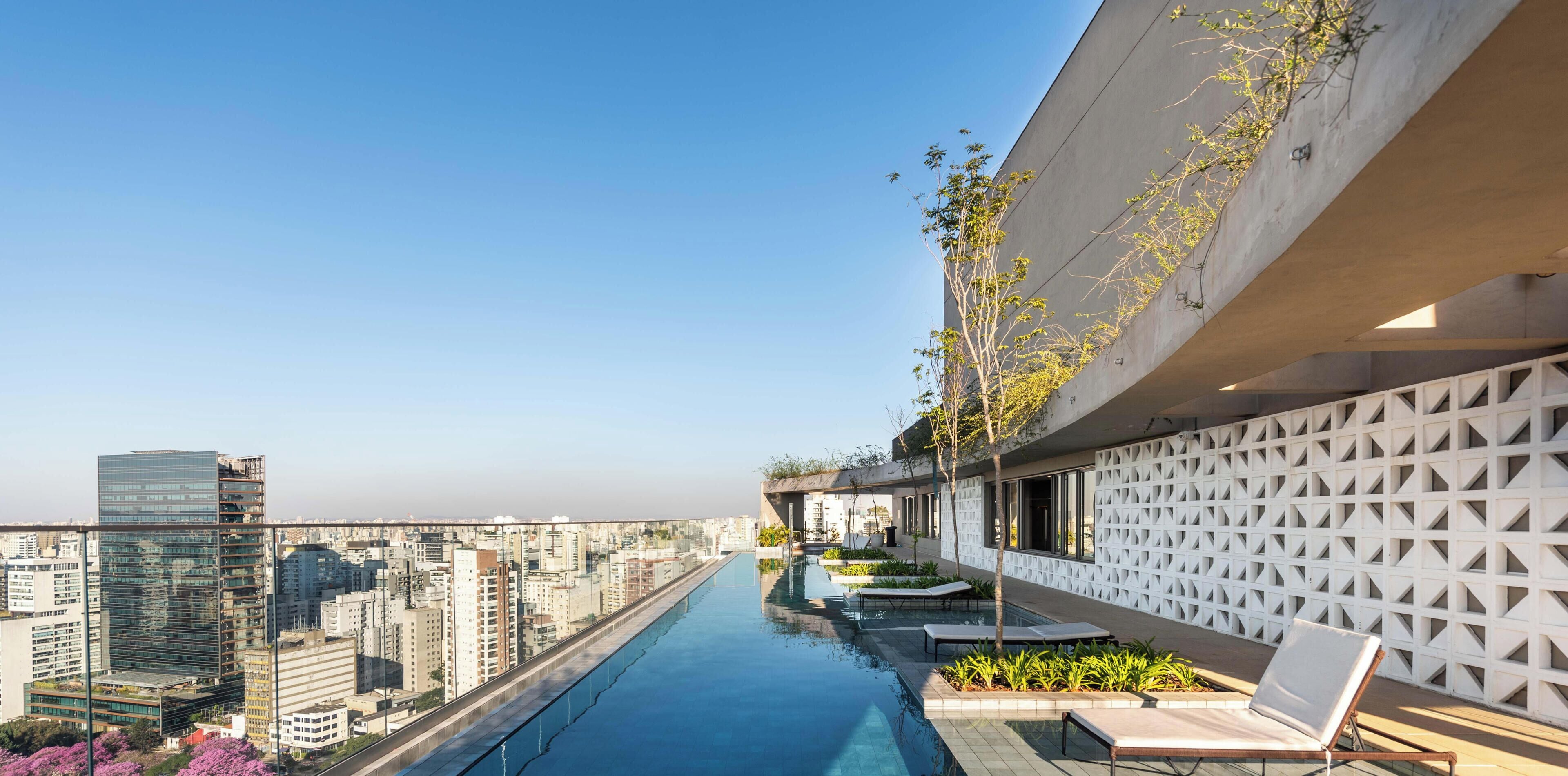 Una piscina sul tetto con vista sulla città, una parete geometrica e poltrone relax.
