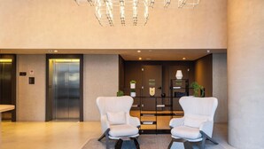 A modern lobby with two white armchairs, a geometric floor rug, a wall-mounted light fixture, and a reception desk. - Ária Higienópolis by WeCare Hosting (São Paulo)
