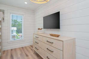 Un intérieur moderne avec un meuble en bois, un téléviseur à écran plat fixé au mur et une fenêtre équipée de stores.