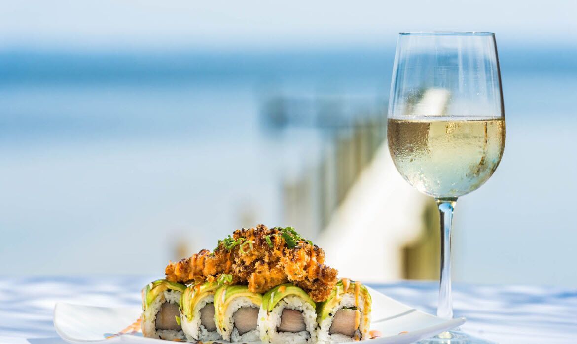 A sushi dish with a glass of white wine on a table with a blurred background.