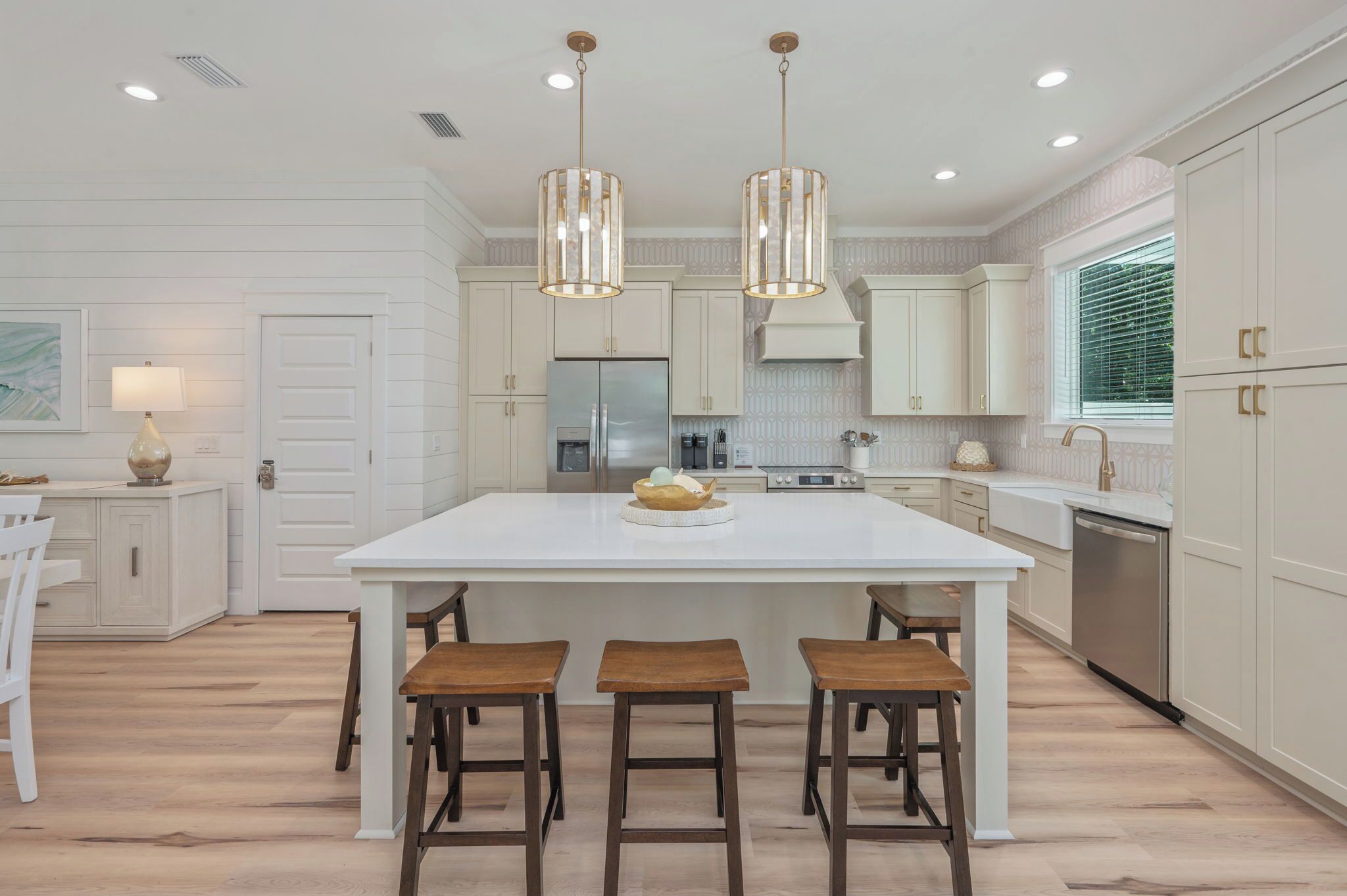 A modern kitchen with a central island, pendant lights, and wooden stools.