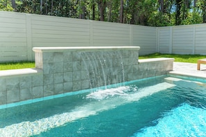 A swimming pool with a waterfall feature, surrounded by a white fence and greenery. - Seahorse: New 30A beach home! 1.6 miles to Seaside (Santa Rosa Beach)