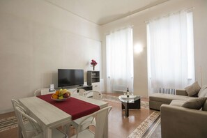 Ein Wohnzimmer mit Esstisch, einer Couch, einem Fernseher und einer Heizung.