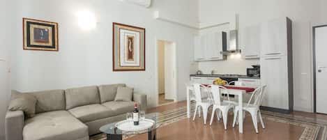A living room with a sofa, a glass coffee table, and a dining area with chairs and a table.