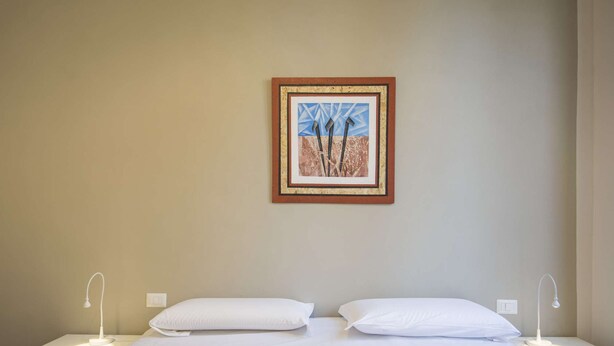 Ein Hotelzimmer mit Bett, zwei Nachttischen, einem Wandbild und einem Lichtschalter.