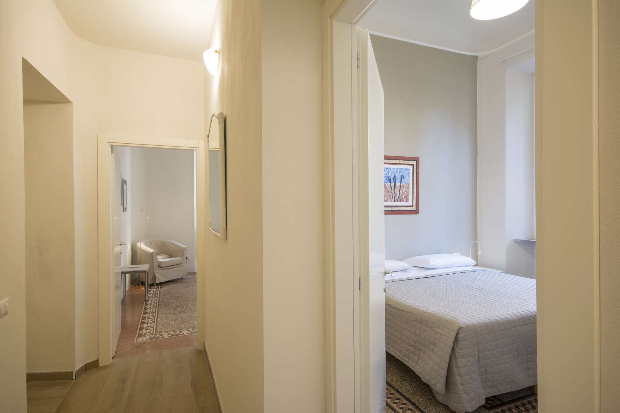 A hotel room with a bed, a chair, a small table, and a door leading to another room.