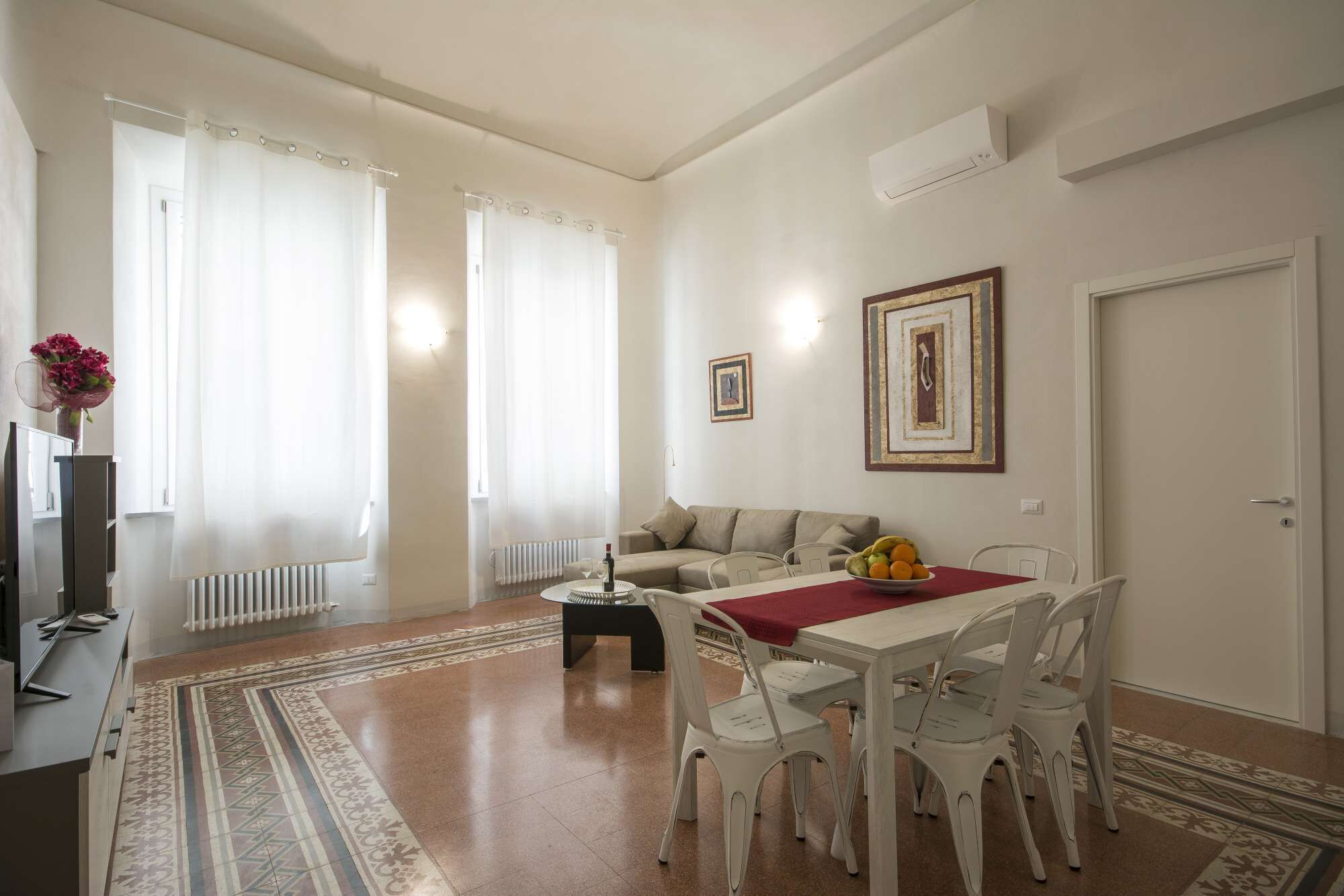 Een woonkamer met een bank, een eettafel met stoelen, een radiator en een deur.