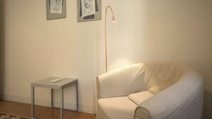 Ein schlicht eingerichteter Raum mit einer Couch, einem kleinen Tisch und zwei gerahmten Kunstwerken an der Wand.