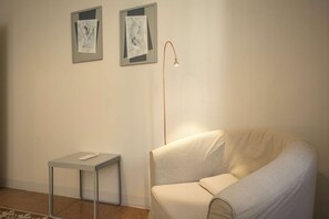 Ein schlicht eingerichteter Raum mit einer Couch, einem kleinen Tisch und zwei gerahmten Kunstwerken an der Wand.